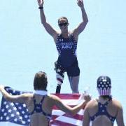 Melissa Stockwell, in stars-and-stripes track wear, with arms extended above her head, faces two people holding an American flag. (Wikimedia Commons/Tânia Rêgo/Agência Brasil)