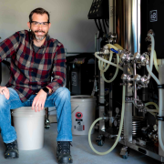 Man in flannel shirt wearing safety glasses sits next to equipment with lots of tubes